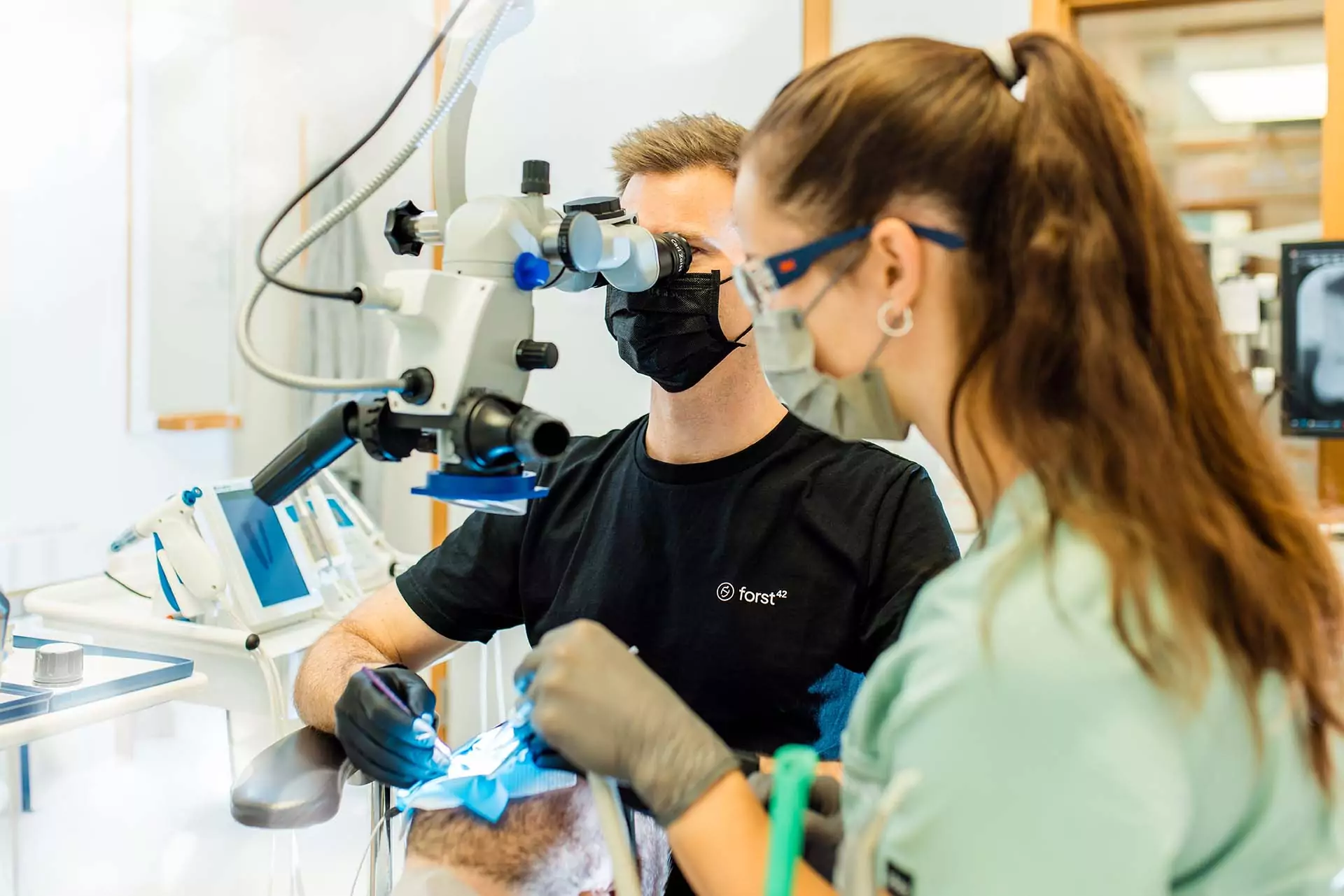 forst42 Wurzelbehandlung Zahnrettung Arzt operiert mit Mikroskop im Mund eines Patienten